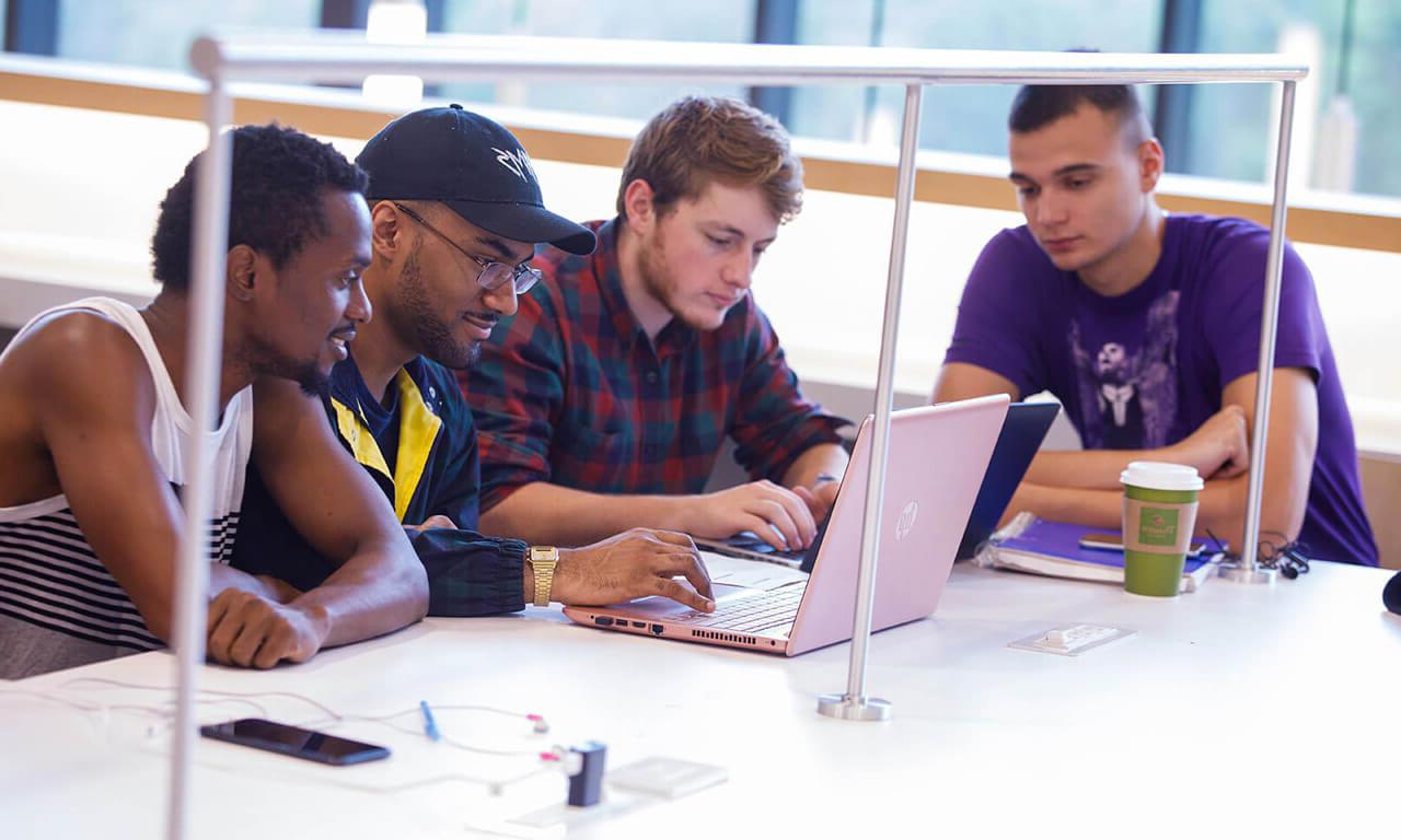 students in the library gathered around a laptop